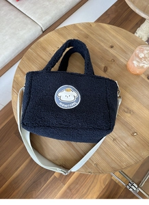 Detail of black faux shearling tote bag with cartoon embroidery and wide white shoulder strap