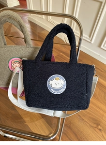 Plush lamb wool crossbody bags in black and olive green on a modern chair