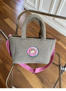 Detail of grey lamb wool tote bag with cartoon patch and pink woven shoulder strap