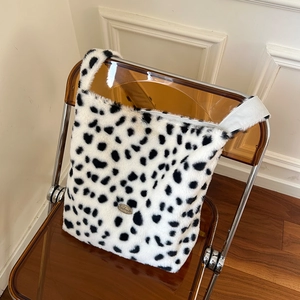 Plush faux fur cow print tote bag with handmade metal plaque on a modern chair