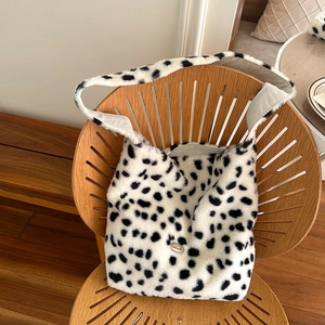 Faux fur tote bag with cow print pattern and handmade metal tag on a designer chair