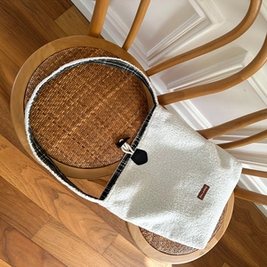Close-up of white plush crossbody bag with checkered strap on a wooden rattan chair