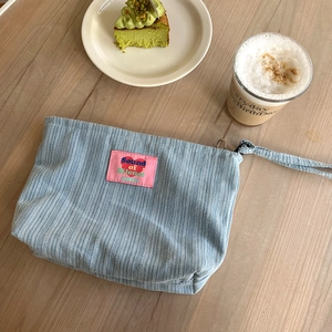 Detailed shot of a blue corduroy makeup bag with pink patch on a cozy wooden table