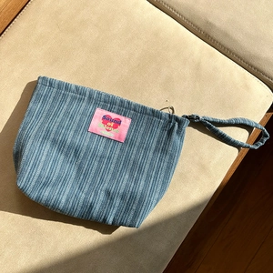 Detail of blue striped fabric makeup bag with pink label and wrist strap on sofa