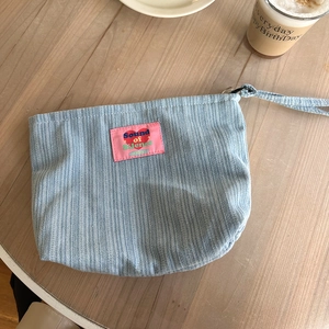 Blue striped denim toiletry bag with pink label shown on a wooden desk with a latte