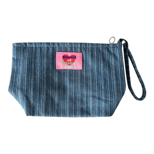 Blue denim striped cosmetic bag with heart patch and wrist strap on white background