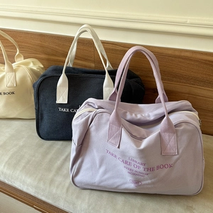 Three canvas boston bags in beige, black, and purple neatly displayed on a bench