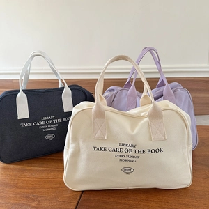 Three canvas Boston bags in beige, black and lilac displayed on a wooden surface