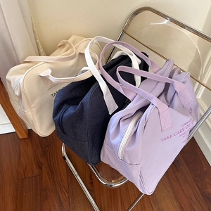 Detailed view of canvas Boston bags in beige, navy blue, and purple on a chair