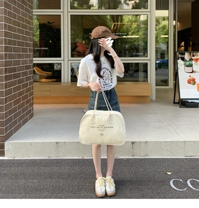 Detail of a large canvas Boston bag with letter print shown in a street style setting