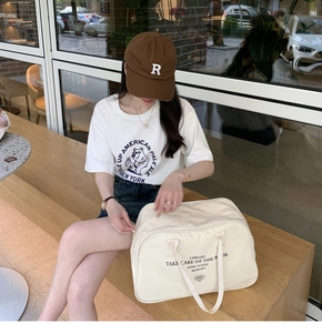 Large off-white canvas Boston travel bag with black LIBRARY lettering shown on a model