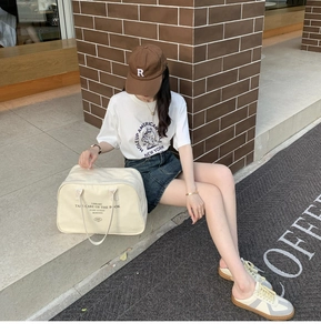 Outdoor shot of a cream canvas Boston bag styled with a bear T-shirt and denim skirt
