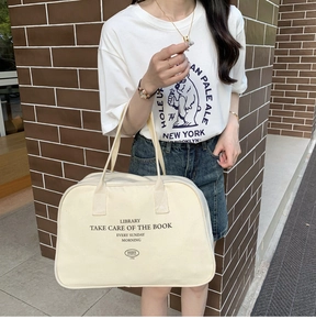 Detail of a large beige canvas Boston bag with black lettering held by a model