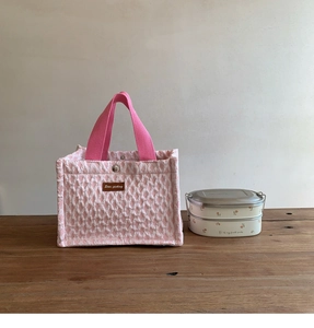 Detail showing pink popcorn fabric texture and leather logo on the portable lunch bag