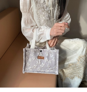 Detail of light purple embroidered lunch bag with white floral lace and leather logo tag