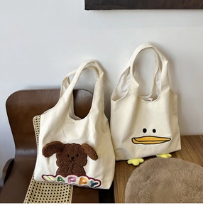 Detail of canvas tote bags featuring plush dog embroidery and cute 3D duck feet accents