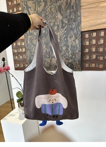 Detailed view of a brown canvas tote bag featuring a cute cartoon cake and blue 3D legs