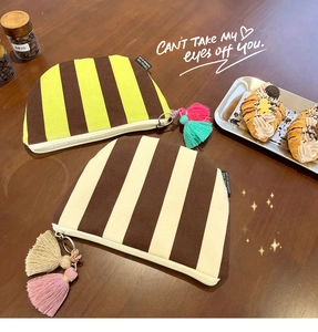 Detail of striped canvas makeup bags with decorative tassels on a wooden table