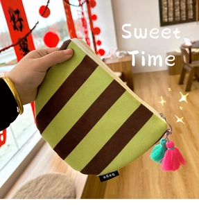 Close-up of green and brown striped canvas makeup bag with a colorful tassel detail