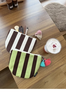 Detail of striped canvas makeup bags with decorative tassels on a wooden desktop