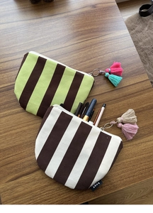 Close-up of striped canvas cosmetic bags with colorful tassels and makeup tools on wood