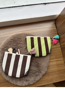 Top view of striped canvas makeup bags with colorful tassels on a plush mat