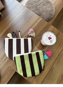 Detail of striped canvas makeup bags with colorful tassels on a wooden surface