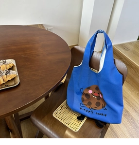 Close-up of Klein blue canvas tote bag with happy cookie print on a wooden chair