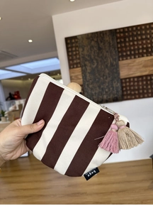 Detailed texture of striped canvas makeup bag with a decorative tassel and zipper