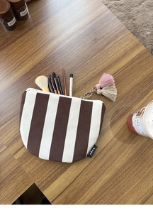 Detail of striped canvas makeup bag with metal zipper and two-tone tassel pendant