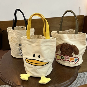 Detailed view of three canvas tote bags with cute cartoon embroidery on a wooden table