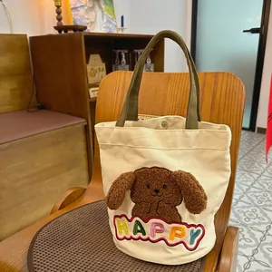 Cute off-white canvas handbag with 3D dog embroidery and green handles on wooden chair