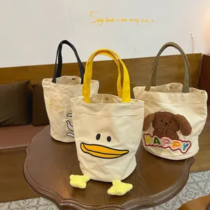 Three cute cartoon canvas bucket bags with embroidery on a wooden table for daily use