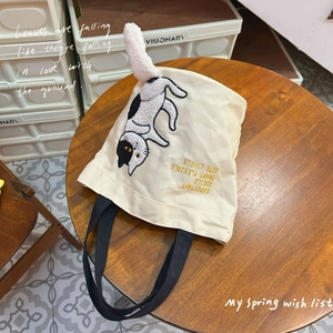 Cream canvas tote bag with 3D cat embroidery and plush tail on a wooden table