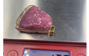 Close-up of fuchsia druzy stone pendant with gold metal edges on a digital scale