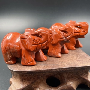 Drie handgesneden rode jaspis olifantenbeelden op een decoratieve houten standaard