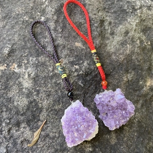 Ciondolo in grappolo di ametista naturale grezza con corda tessuta a mano su sfondo di roccia