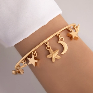 Détail du bracelet doré avec pendentifs étoile et lune porté avec chemise blanche