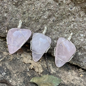 Trois pendentifs en quartz rose enroulés de fil argenté sur fond de pierre naturelle