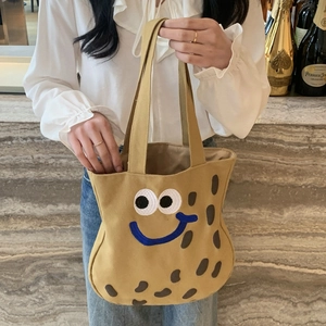 Dettaglio del ricamo con faccina blu sorridente su una borsa tote in tela gialla