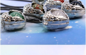 Close-up of angel wing lockets with various colorful gemstones and black cords