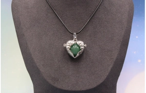 Close-up of vintage angel wings heart locket with faceted green stone on a black cord