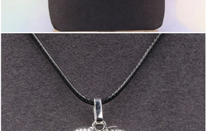 Detailed close-up of heart locket pendant with radial texture on black woven cord