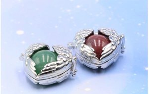 Macro detail of silver angel wing heart locket pendants with green and red gemstones
