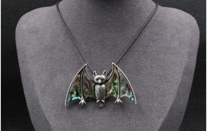 Macro detail of bat pendant with iridescent abalone shell inlay on vintage silver metal