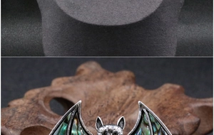 Macro shot of silver-toned bat brooch with iridescent green and blue abalone shell inlay