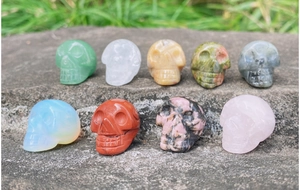 Detailed collection of nine hand-carved natural crystal mini skulls on grey stone
