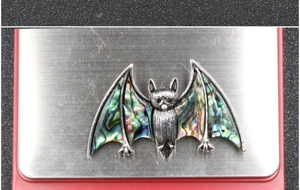 Macro detail of bat-shaped brooch with colorful abalone shell inlays and silver metal wings