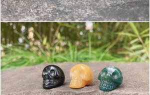 Three small hand-carved crystal skulls in obsidian and agate on a stone surface