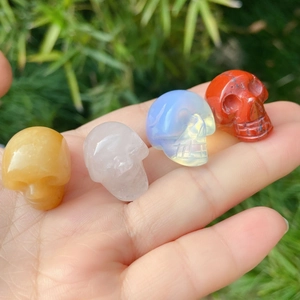 Set of four mini carved crystal skulls in various gemstones held in a hand